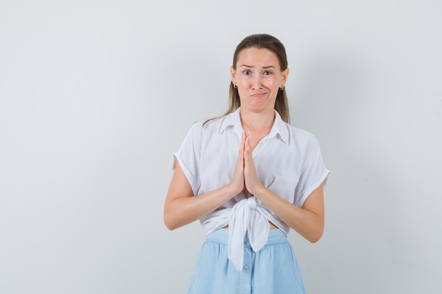 Jonge dame in blouse en rok die namastegebaar toont en twijfelachtig kijkt