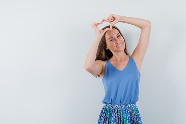 Jonge dame in blouse, rok die vredesgebaar boven het hoofd toont en gelukkig, vooraanzicht kijkt. ruimte voor tekst