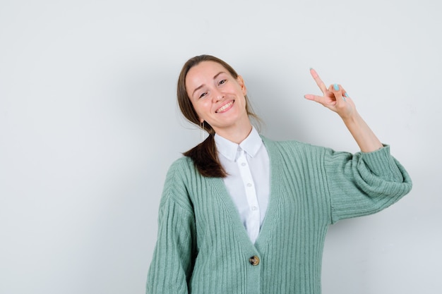 Jonge dame in blouse, vest met v-teken en blij, vooraanzicht.