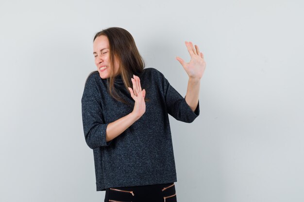 Jonge dame in casual overhemd handen opheffen om zichzelf te verdedigen en bang kijken