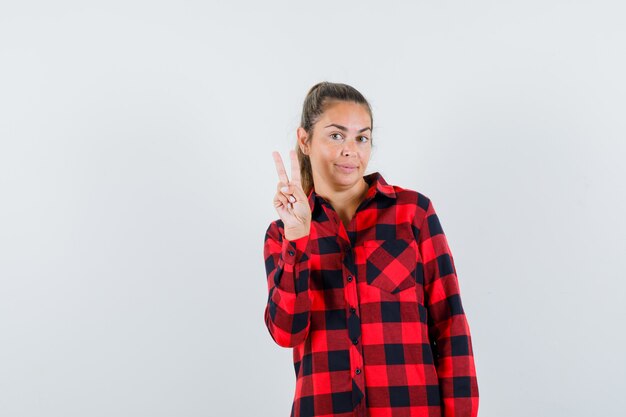 Jonge dame in casual shirt met overwinningsteken en op zoek naar zelfverzekerd, vooraanzicht.