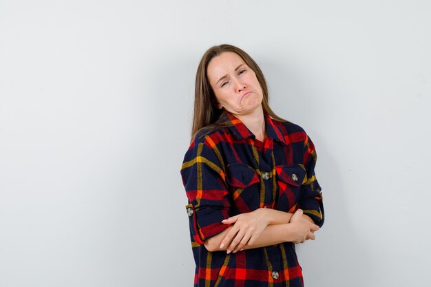 Jonge dame in casual shirt staande met gekruiste armen en op zoek verontrust, vooraanzicht.