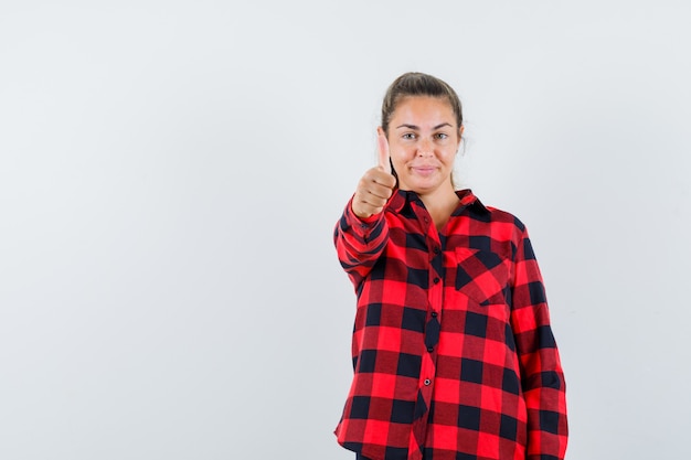 Gratis foto jonge dame in gecontroleerd overhemd duim opdagen en vrolijk kijken