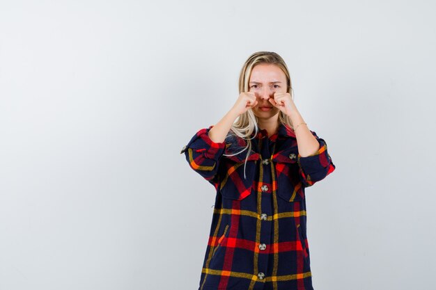 Jonge dame in geruit overhemd die ogen wrijven en beledigd, vooraanzicht kijken.