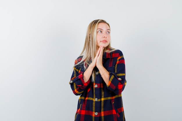 Gratis foto jonge dame in geruit overhemd die vingers samen drukken om te bidden en vreedzaam, vooraanzicht kijken.