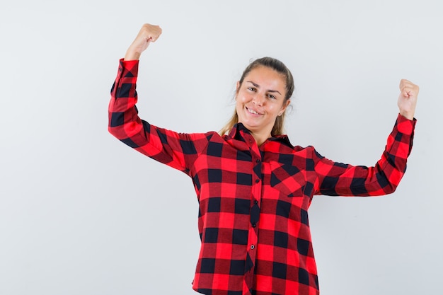 Jonge dame in geruit overhemd die winnaargebaar tonen en gelukkig kijken