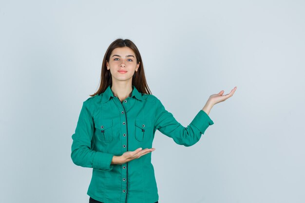 Jonge dame in groen overhemd die verwelkomend gebaar tonen en zelfverzekerd, vooraanzicht kijken.