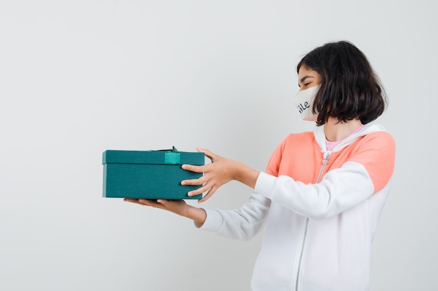 Jonge dame in hoodie, de giftdoos van de gezichtsmaskerholding en het kijken gelukkig.