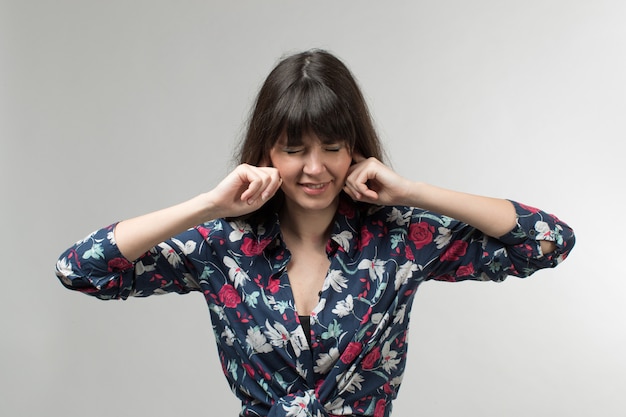 jonge dame in ontworpen t-shirt sluit haar oren met lang haar op wit