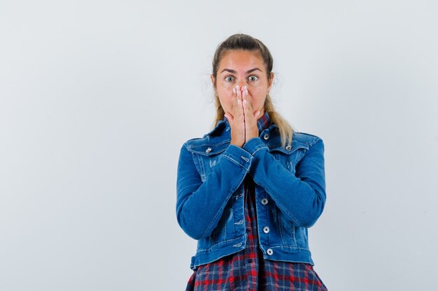 Jonge dame in overhemd, jasje hand in hand op mond en op zoek angstig, vooraanzicht.