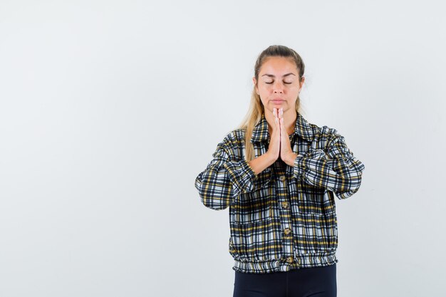 Jonge dame in overhemd, korte broek die namaste-gebaar toont en ontspannen, vooraanzicht kijkt.