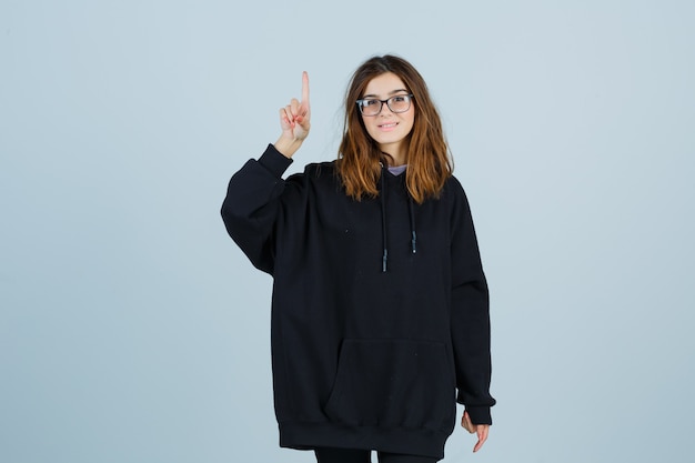 Jonge dame in oversized hoodie, broek die op en neer wijst en er gelukkig uitziet, vooraanzicht.