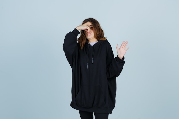 Jonge dame in oversized hoodie, broek knijpt neus vanwege slechte geur en walgt op zoek, vooraanzicht.