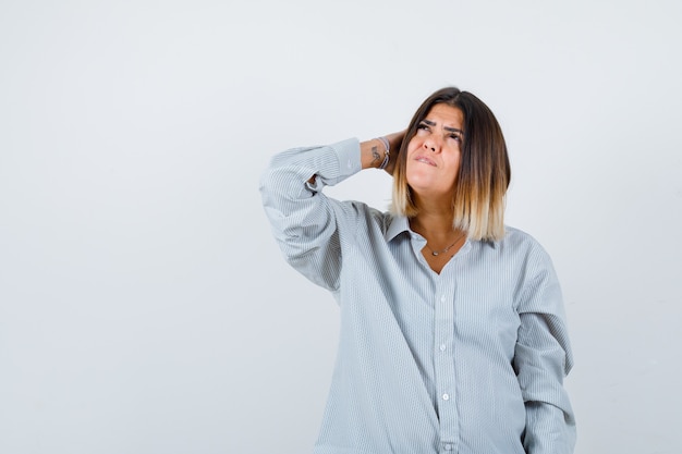 Jonge dame in oversized shirt die hand op het hoofd houdt en er attent uitziet, vooraanzicht.