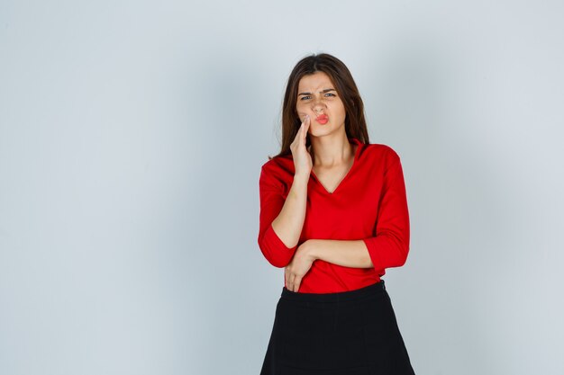 Jonge dame in rode blouse, rok die aan kiespijn lijdt en onwel kijkt