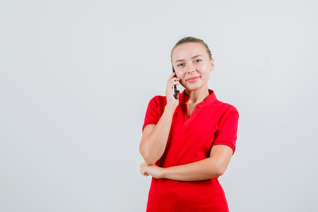 Jonge dame in rood t-shirt die op mobiele telefoon spreekt en vrolijk kijkt