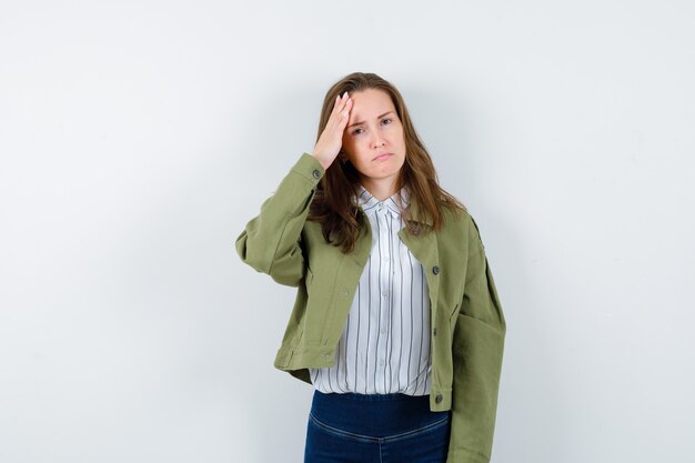 Jonge dame in shirt die hand op het hoofd houdt en er verdrietig uitziet, vooraanzicht.