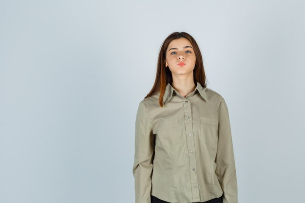 Jonge dame in shirt die wangen blaast, lippen pruilt en verbaasd kijkt, vooraanzicht.
