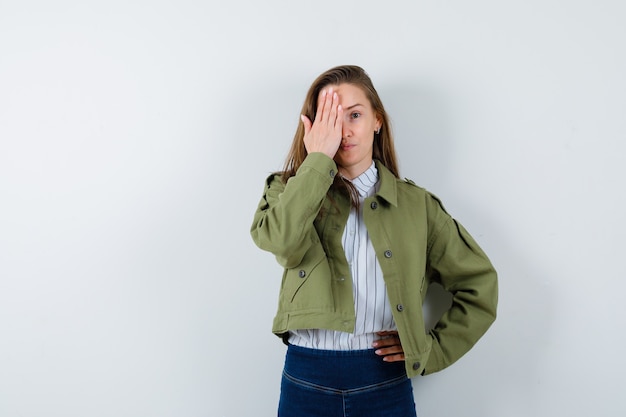 Jonge dame in shirt, jas die hand op oog houdt en er schattig uitziet, vooraanzicht.