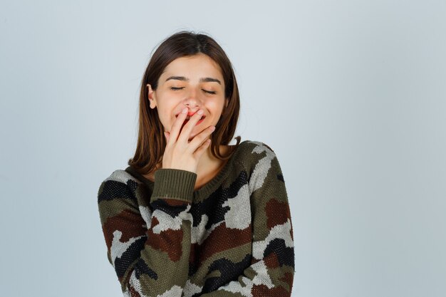 Jonge dame in sweater, rok die hand op mond houdt en vrolijk kijkt