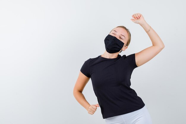 Jonge dame in t-shirt, broek, medisch masker dat geïsoleerd winnaargebaar toont