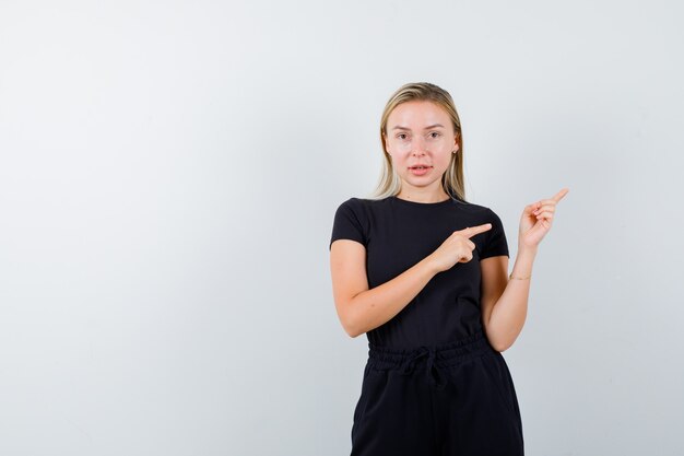 Jonge dame in t-shirt, broek wijst naar de rechterbovenhoek en kijkt besluiteloos, vooraanzicht.