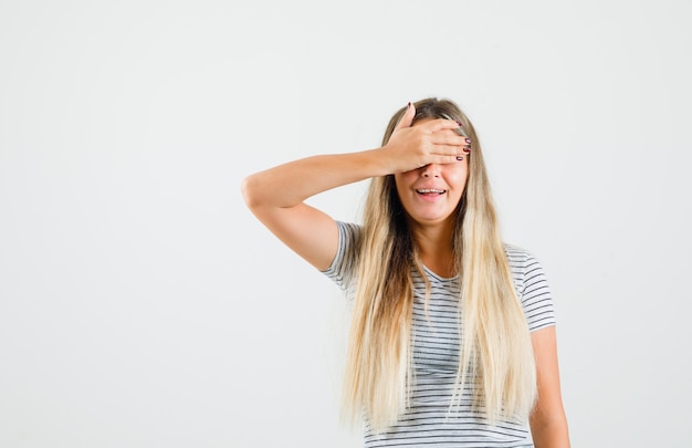 Jonge dame in t-shirt die hand op haar ogen houdt en opgewonden, vooraanzicht kijkt.