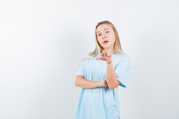 Jonge dame in t-shirt die iemand vooruit wenkt en zelfverzekerd kijkt, vooraanzicht.