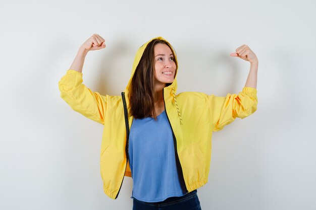 Jonge dame in t-shirt, jas die winnaargebaar toont en er gelukkig uitziet, vooraanzicht.