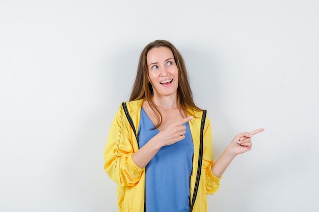 Jonge dame in t-shirt, jas wijst naar de rechterkant en ziet er dromerig uit, vooraanzicht.