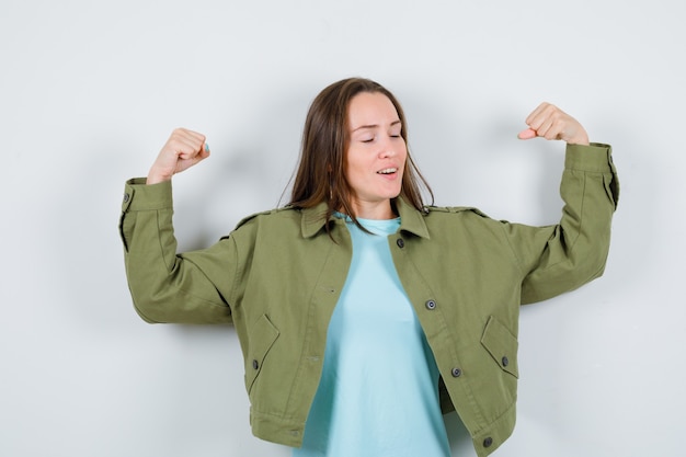 Gratis foto jonge dame in t-shirt, jasje met spieren van armen en op zoek trots, vooraanzicht.