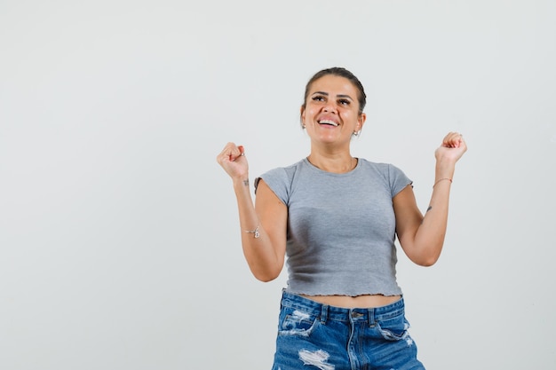 Jonge dame in t-shirt, korte broek die winnaargebaar toont en gelukkig kijkt