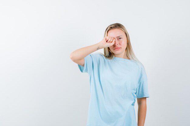 Jonge dame in t-shirt oog wrijven en op zoek beledigd, vooraanzicht.