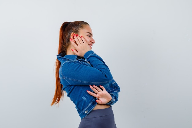 Jonge dame in top, spijkerjasje met hand op wang en vrolijk, vooraanzicht.