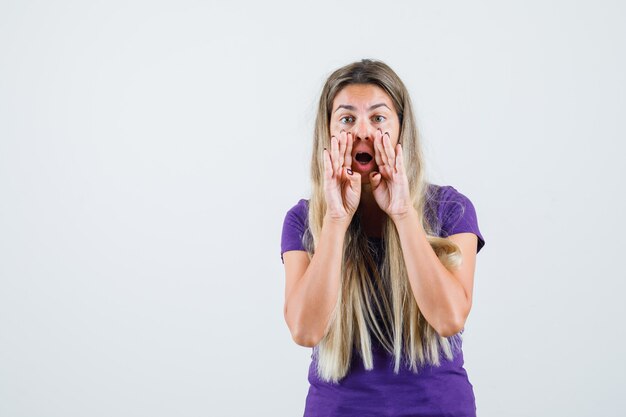 Jonge dame in violet t-shirt geheim vertellen met handen dichtbij mond, vooraanzicht.