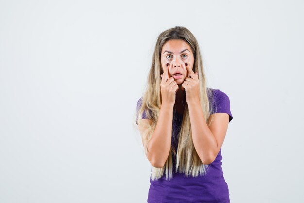 Jonge dame in violet t-shirt oogleden naar beneden trekken met vingers, vooraanzicht.