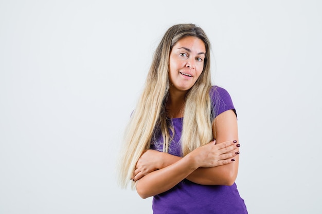 Jonge dame in violet t-shirt zichzelf knuffelen en op zoek naar mooi, vooraanzicht.