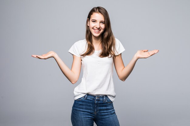 Jonge dame in wit t-shirt en spijkerbroek armen aan verschillende kanten voor witte studio achtergrond