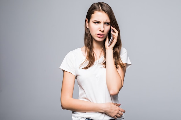 Jonge dame in wit t-shirt en spijkerbroek praat over haar telefoon voor witte studio achtergrond