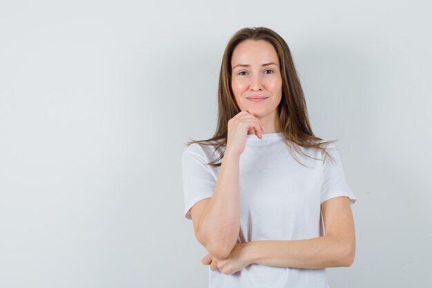 Jonge dame in wit t-shirt staande in denken pose en op zoek verstandig