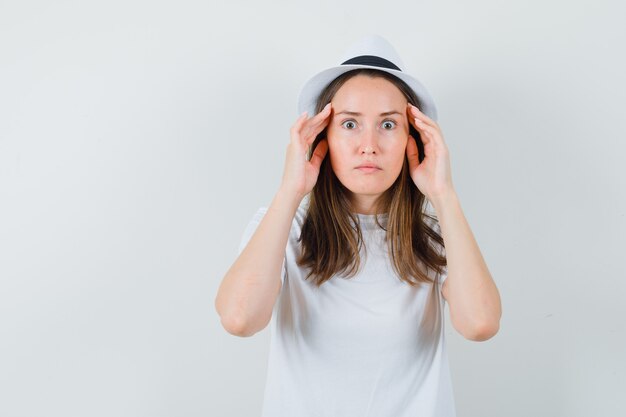 Jonge dame in witte t-shirthoed die handen op tempels houdt en verbaasd kijkt