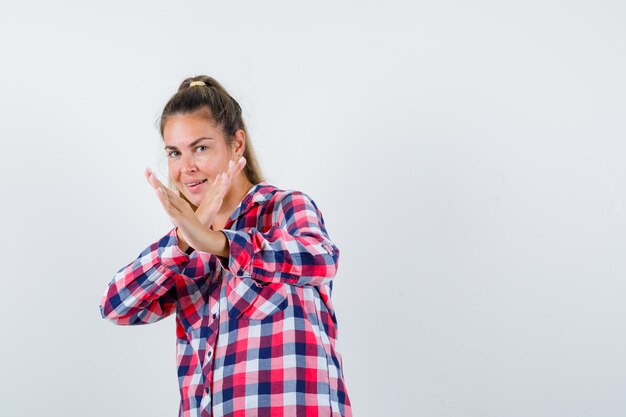 Jonge dame karate hakken gebaar in ingecheckte shirt tonen en op zoek zelfverzekerd. vooraanzicht.