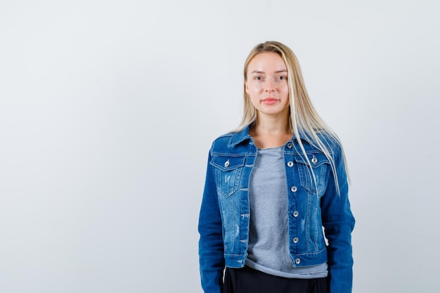 Jonge dame kijkt naar camera in t-shirt, spijkerjasje, rok en ziet er prachtig uit