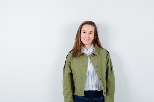 Jonge dame kijkt naar de camera in shirt, jas en ziet er boeiend uit, vooraanzicht.