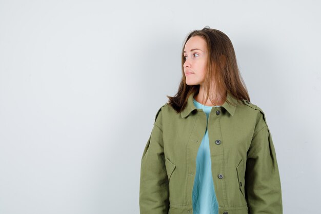 Jonge dame kijkt weg in t-shirt, jas en kijkt peinzend, vooraanzicht.