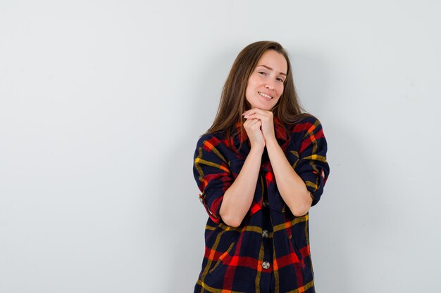 Jonge dame kin op gevouwen handen in casual shirt steunen en op zoek naar delicaat, vooraanzicht.