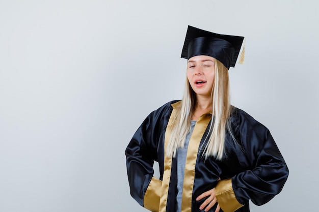 Jonge dame knippert naar de camera in academische jurk en ziet er zelfverzekerd uit.