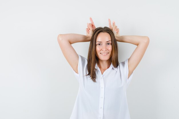 Gratis foto jonge dame konijntje gebaar maken op haar hoofd in witte blouse en grappig op zoek