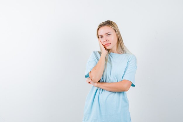 Jonge dame kussen gezicht op haar hand in t-shirt en op zoek attent, vooraanzicht.