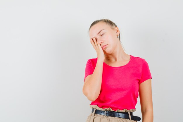 Jonge dame leunend gezicht op palm in roze t-shirt en broek en op zoek slaperig